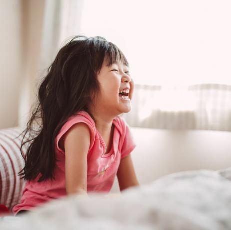 छोटी लड़की बिस्तर पर ख़ुशी से हँस रही है