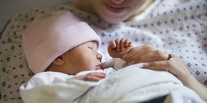 गुलाबी टोपी में कंबल में लिपटी नवजात बच्ची, ठुड्डी से नीचे तक अस्पताल का गाउन पहने मां उसे थामे हुए दिख रही है