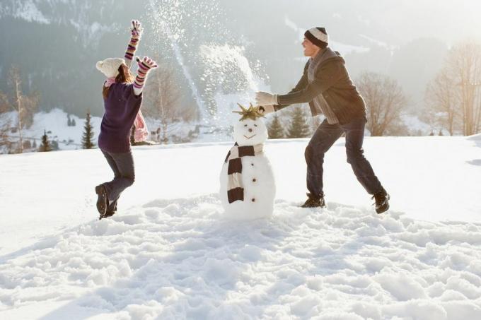 युगल स्नोमैन बना रहे हैं और बर्फ में खेल रहे हैं