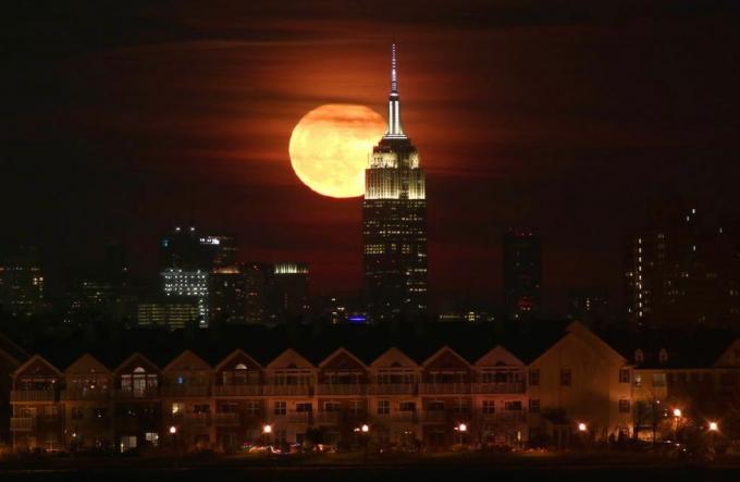 न्यूयॉर्क शहर में एम्पायर स्टेट बिल्डिंग के पीछे पूर्णिमा का चंद्रमा उगता है