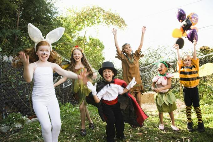 पिछवाड़े में हेलोवीन वेशभूषा में खरगोश, जादूगर, मधुमक्खी, फूल और अन्य के रूप में उत्साहित बच्चे