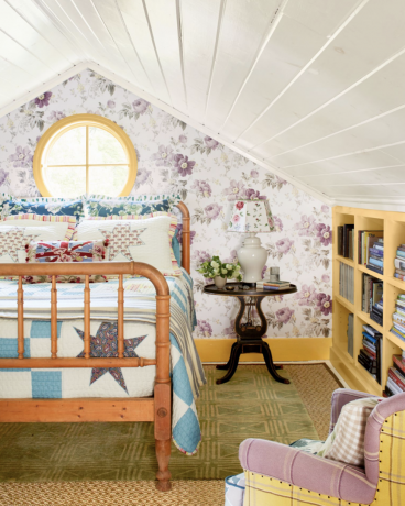 लकड़ी के बिस्तर और हल्के बैंगनी चिंट्ज़ वॉलपेपर के साथ आकर्षक देशी बेडरूम