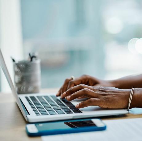 कार्यालय में अकेले लैपटॉप कीबोर्ड पर टाइपिंग करती एक अश्वेत व्यवसायी महिला का क्लोज़अप
