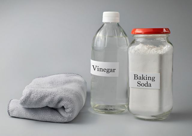 भूरे रंग की पृष्ठभूमि के सामने कांच की बोतल पर सिरका और बेकिंग सोडा के पाठ का क्लोज़अप