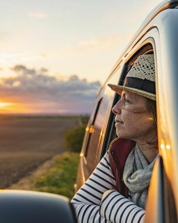 40 साल की एक महिला अपने कैंपेरवन से ग्रामीण इलाकों का नजारा ले रही है, वह संतुष्ट और तनावमुक्त दिख रही है