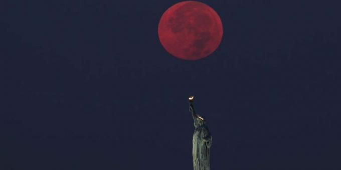 न्यूयॉर्क शहर में स्टैचू ऑफ़ लिबर्टी के पीछे पूर्णिमा का चाँद डूबा हुआ है